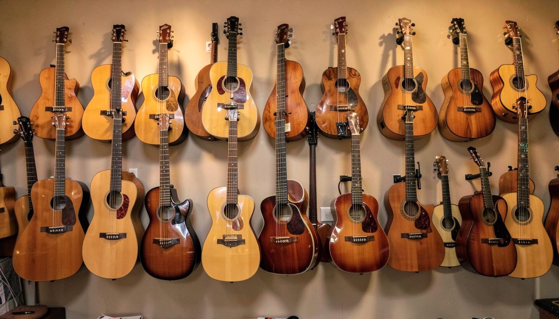 Rows of acoustic and electric guitars hanging on a warmly lit shop wall, rich wood tones against a neutral background.